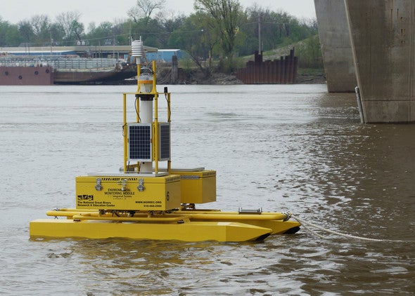 A yellow buoy tests water quality near a bridge