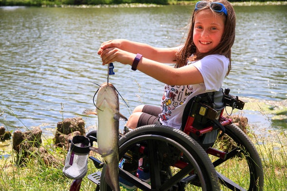 Little girl in wheelchair poses with the catfish she caught