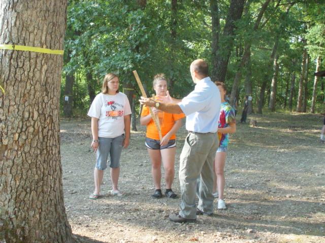 Two young women in shorts and t-shirts receive instruction from a forester.