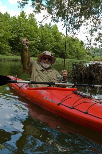 An angler in a bright red kayak holds aloft a fat, 2-pound smallmouth bass.