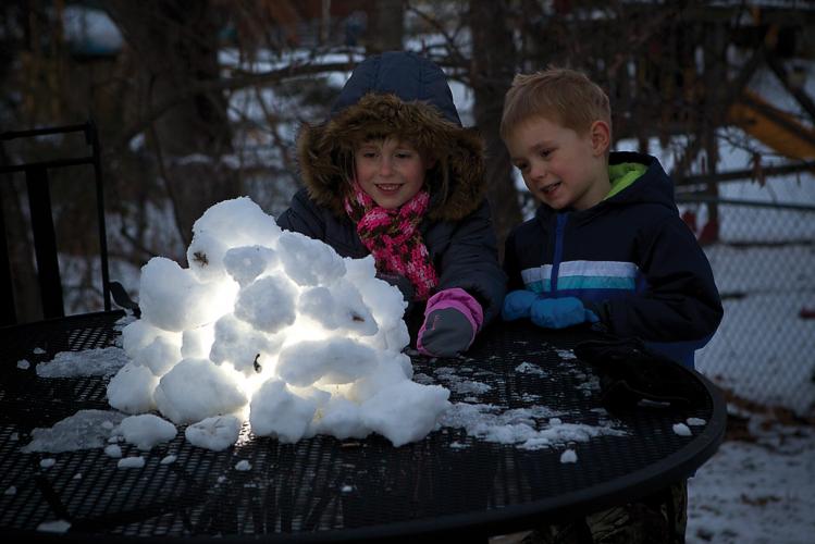 Kids make a snow lantern by piling snow balls around a light.