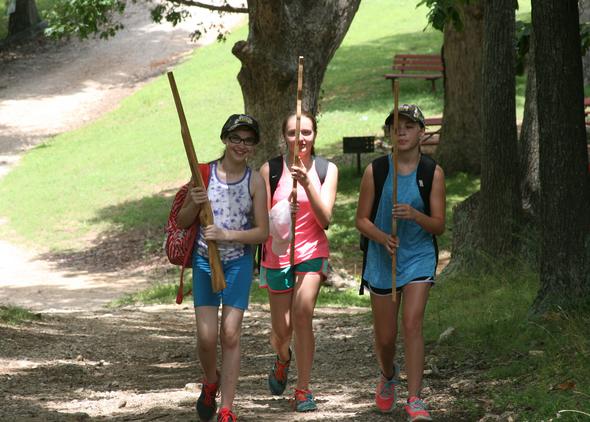 Three girls with practice rifles walk down a trail.