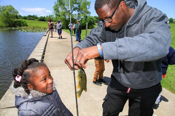 A man helps a little girl take her fish off her line.