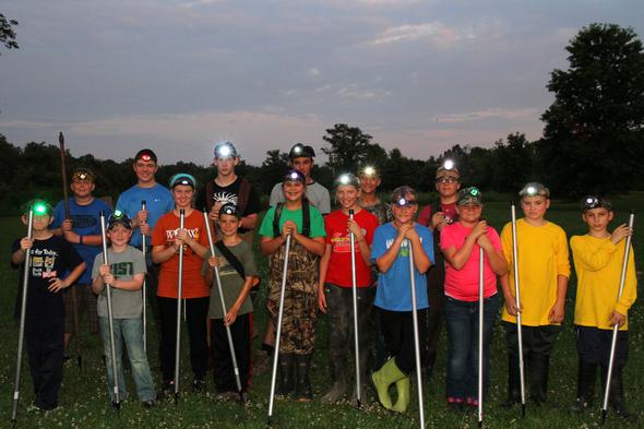 A group of kids preparing to go frog gigging. They have headlamps and are carrying gigs. 