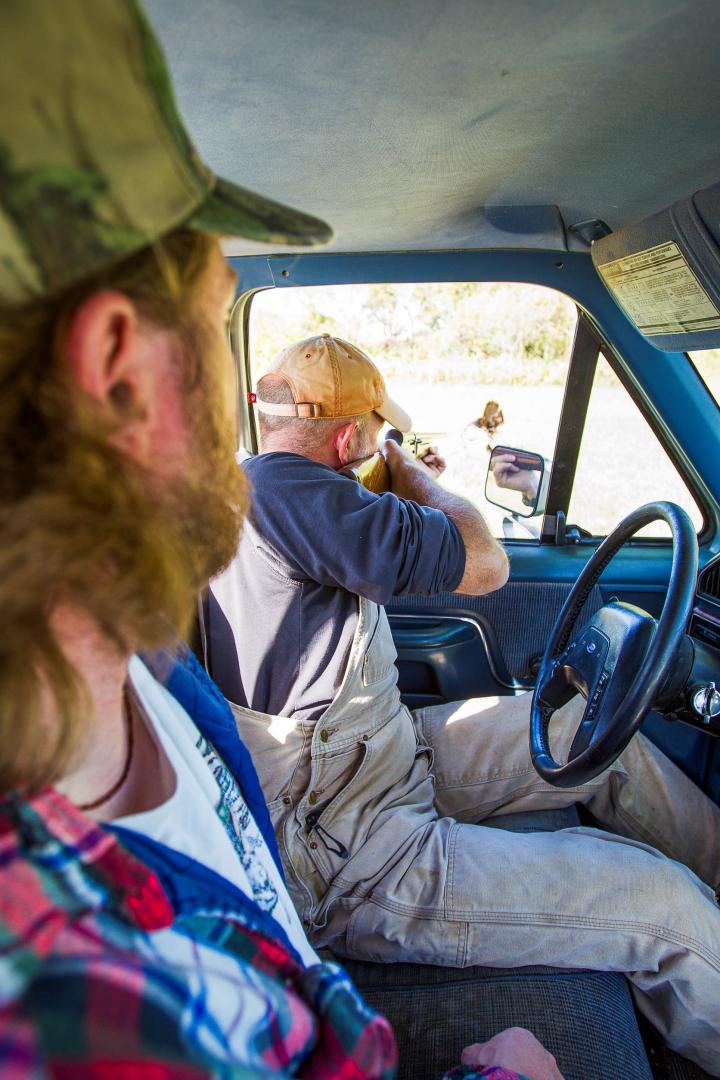 A poacher illegally shoots game from the cab of a pickup truck. another person is in the cab with him.