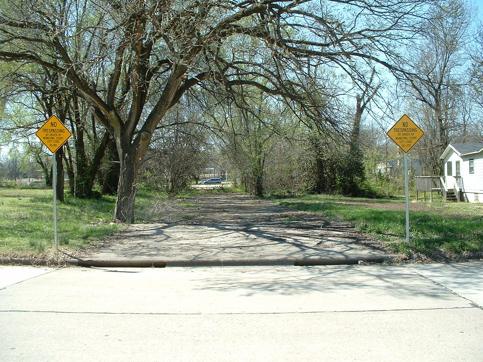 Paved street with trees and grass along it and a "no trespassing" sign on each side