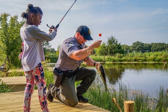 Conservation agent helps little girl reel in a fish.