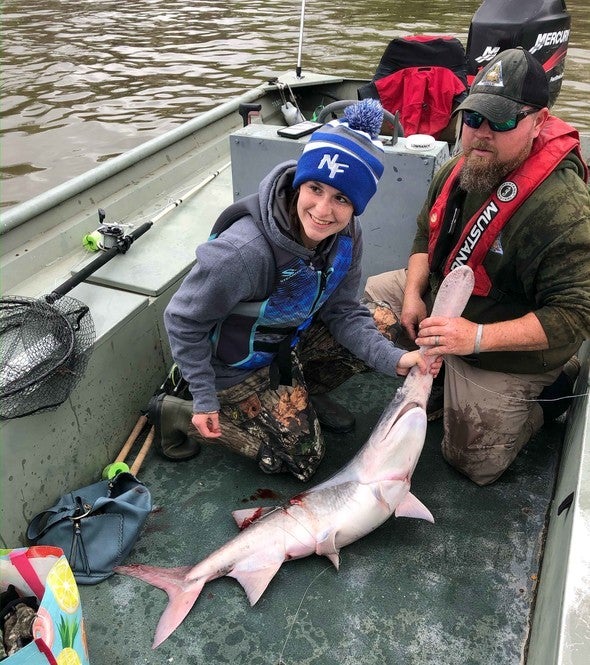 Two people hold snagged paddlefish on boat
