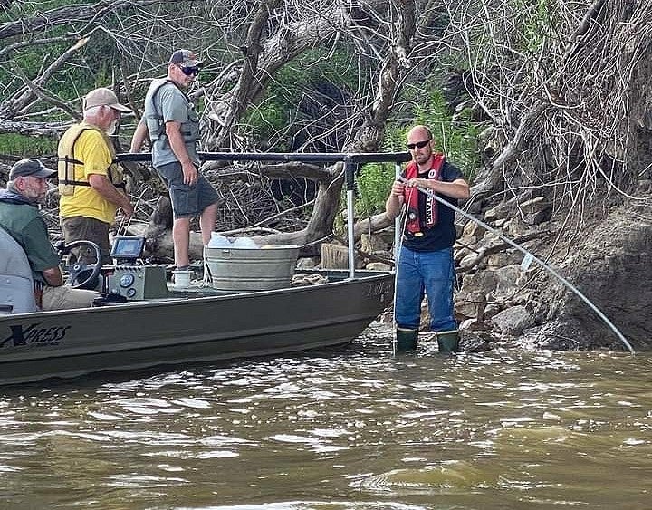 Man checks set line for catfish while two men on a boat watch
