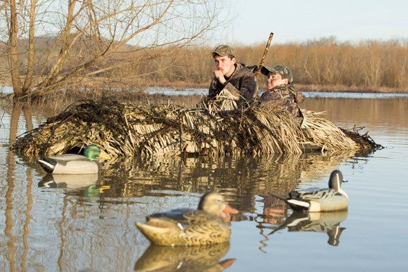 Two duck hunters call from blind