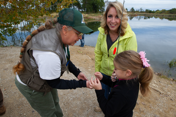 Volunteer helps girl and mother bait fishing hook