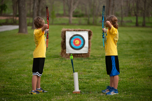 Two young archers aim arrows at outdoor target