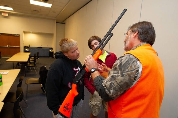 hunter education instructor shows two students a firearm
