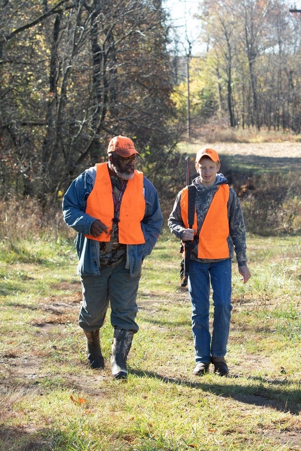 A youth hunter walks with a mentor, both dressed in camouflage and hunter orange,  on a managed hunt in Missouri.