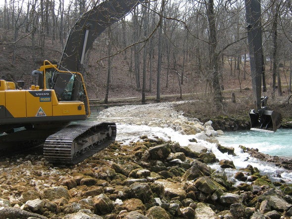 A backhoe moves large boulders to repair a dam