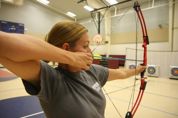 A woman draws back a bow before shooting at a target