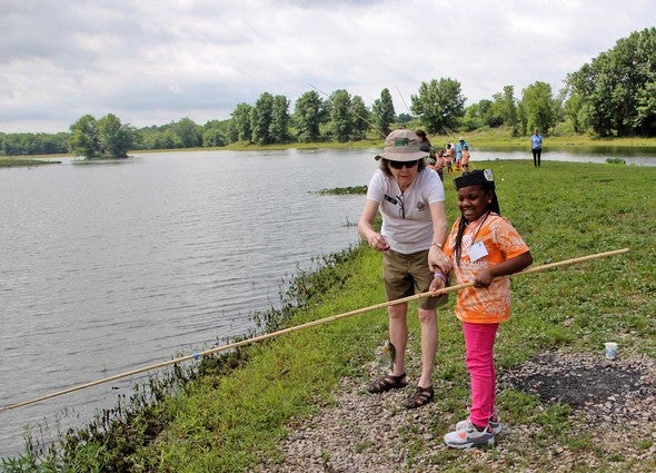 Kid learns to fish at pond with instructor's help