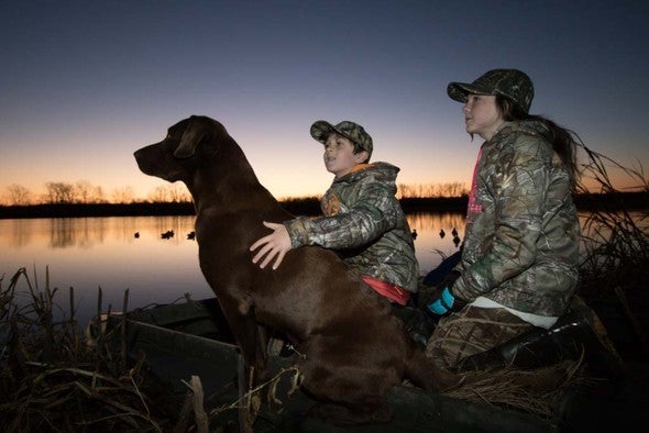 A brother and sister with their dog on a duck hunting trip.