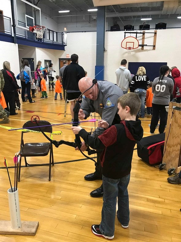Conservation agent teaching youth about archery.