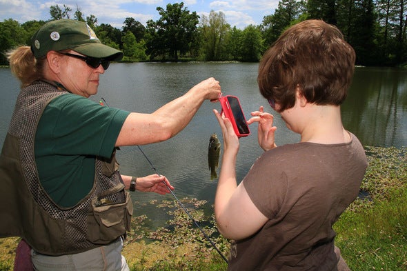 MDC volunteer helps a disabled woman take a picture of the fish she just caught