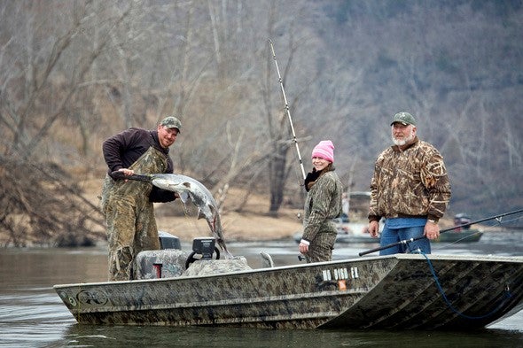 three snaggers haul in a paddlefish to their boat