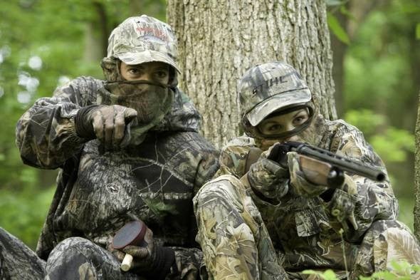 two turkey hunters in camo sitting against tree