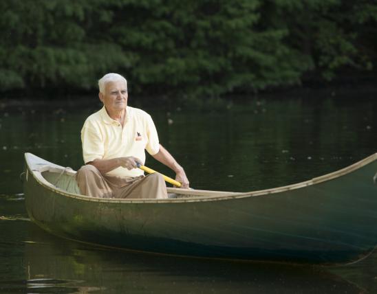 A white-haired man paddles a solo canoe
