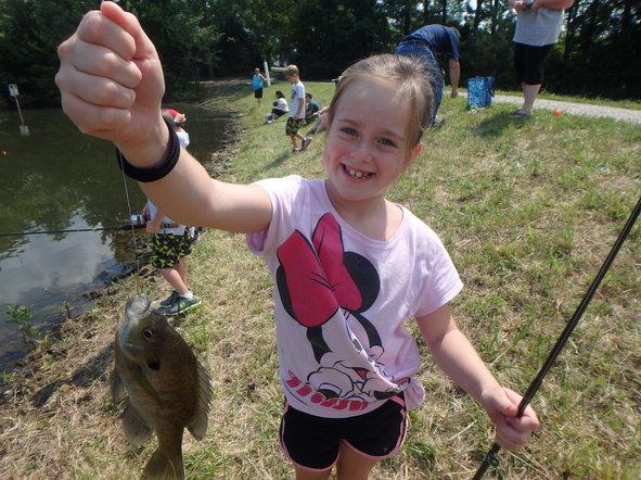A girl in a Minnie Mouse t-shirt proudly holds up a small fish she caught