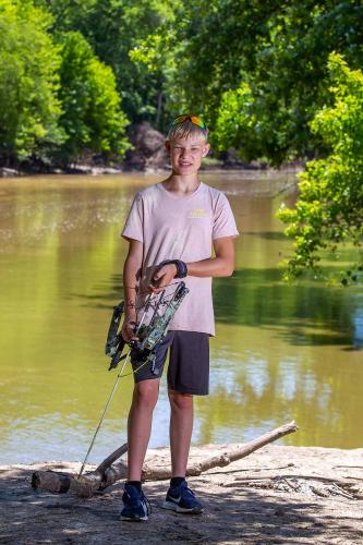 Young bow hunter stands by water