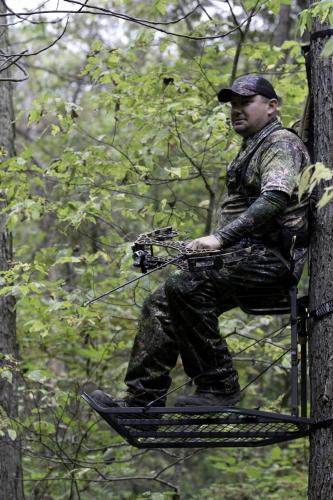 A bowhunter holds his bow in a tree stand.