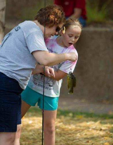 A volunteer helps a girl handle a small sunfish the girl just caught.