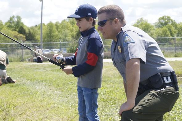 Conservation agent helping a little boy fish.