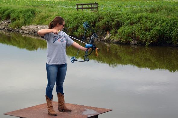 Woman bowfishing into pond