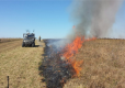 Prescribed burn showing flames along edge of brown, dry grassy field with vehicle and person nearby 