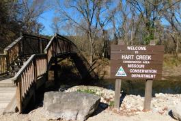 Hart Creek Conservation Area area sign and pedestrian bridge crossing Hart Creek near parking lot