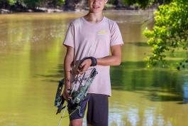 Young bow hunter stands by water