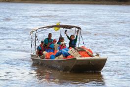 Five volunteers on a boat full of bags of trash during a River Cleanup. One woman has her arms raised in triumph.