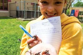 A fourth-grade girl in a yellow sweatshirt holds a handful of slugs and worms