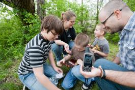 A family with geocache. Someone is holding a GPS unit.