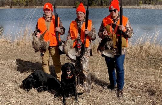 Three women hold pheasant they hunted with two bird dogs