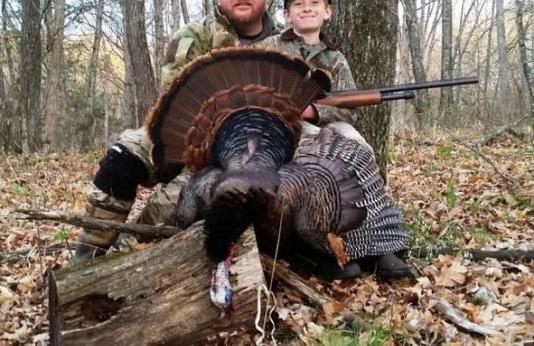 A young hunter and his mentor proudly show off a turkey he harvested. 
