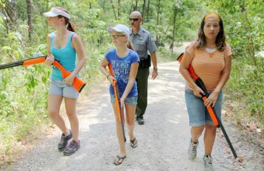 A conservation agent walks with three girls carrying shotguns down a trail. 