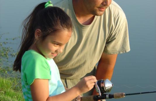 A man watches as his daughter reels in her line.
