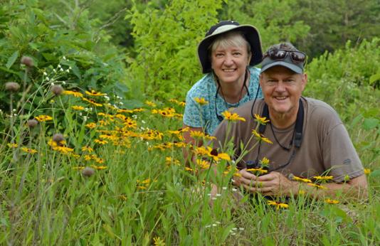 Amy Short and Steve Craig crouch by a flowering plant.