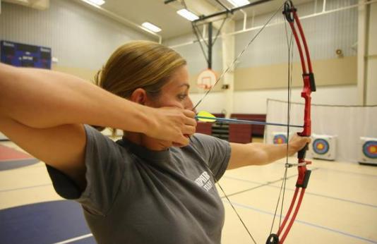 A woman draws back a bow before shooting at a target