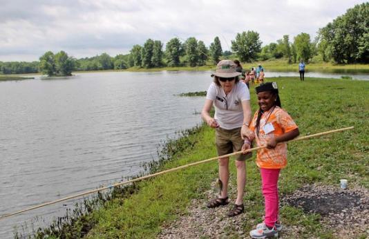Kid learns to fish at pond with instructor's help