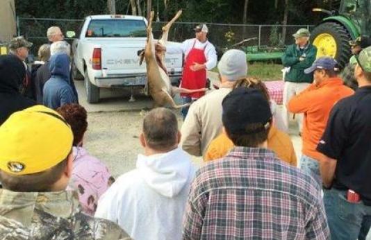 A group of people watch an instructor process a deer