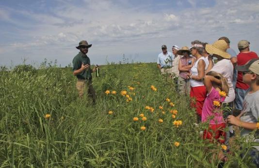 MDC staffer talks to partipants at Prairie Days. He is standing in a prairie with hip-high plants and flowers.