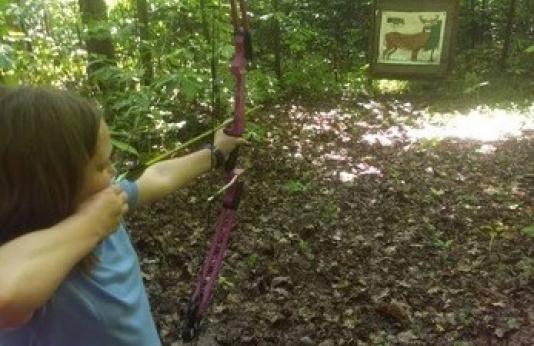 girl shooting bow at target in woods