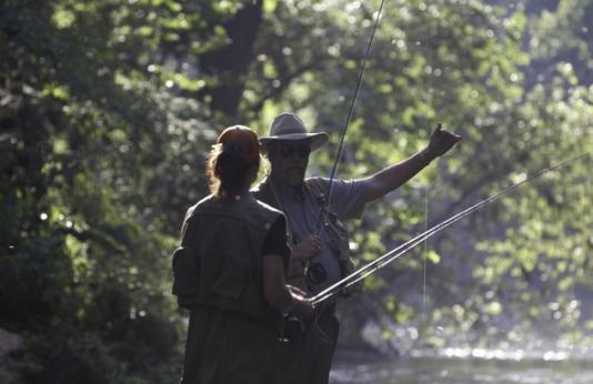 An MDC staff member instructs a woman on fly fishing techniques.